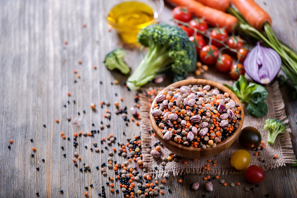 Rohe Bohnen und Linsen in einer Schüssel mit Gemüse daneben