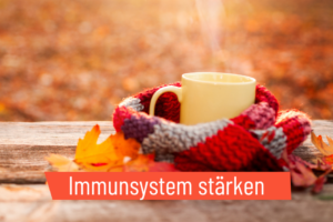 Aus einer Tasse heißem Tee steigt Dampf auf. Die Tasse ist mit einem Schal umwickelt. Herbstliche Stimmung.
